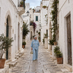 Carolina completo in maglia azzurro, donna che passeggia in un vicolo bianco di un borgo pugliese, maglia con tre bottoni dorati e pantaloni ampi