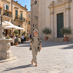 Donna italiana in passeggiata davanti a una chiesa in una piazza, completo tre pezzi tortora con cardigan stampato